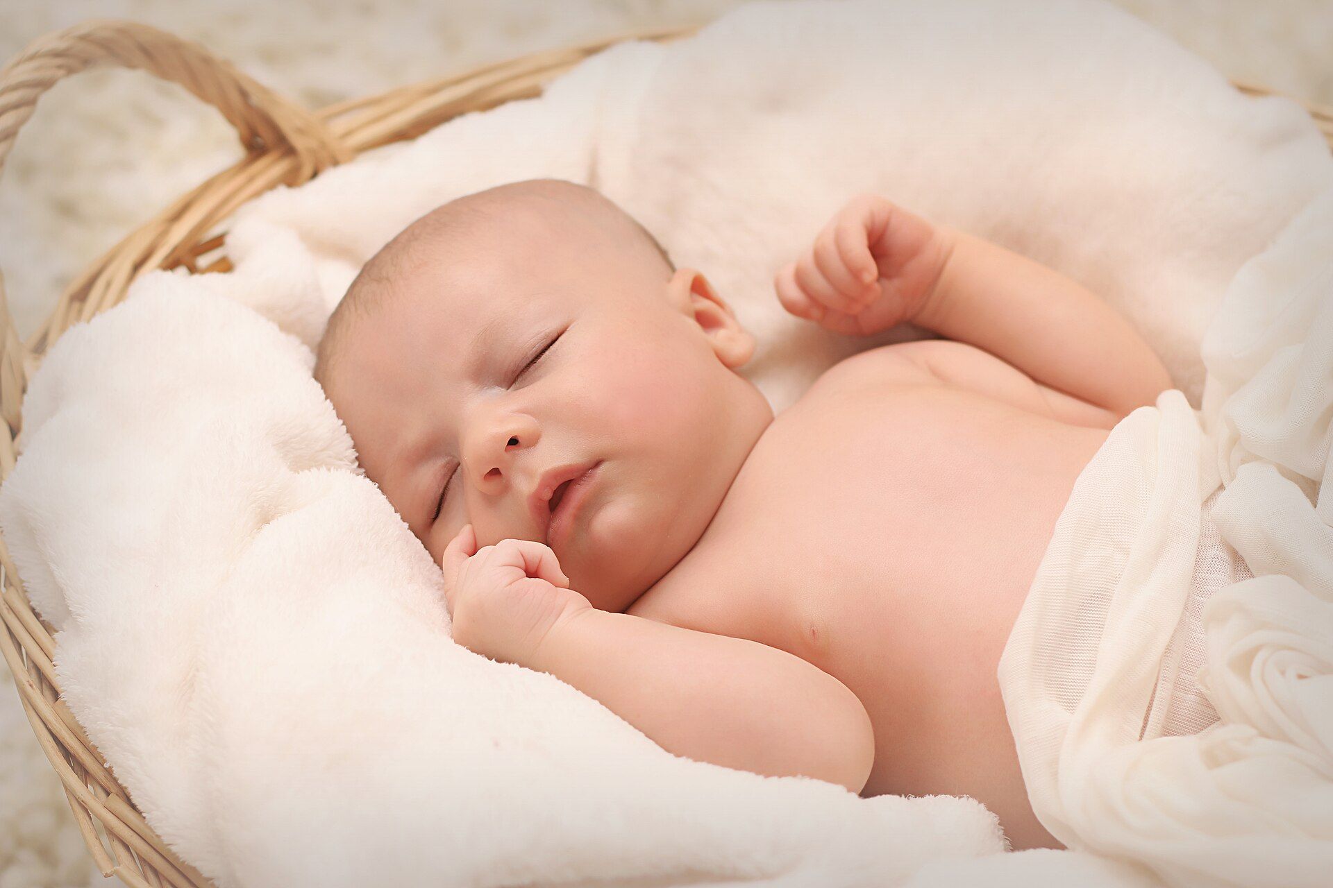 A newborn asleep in a basket lined with a blanket.