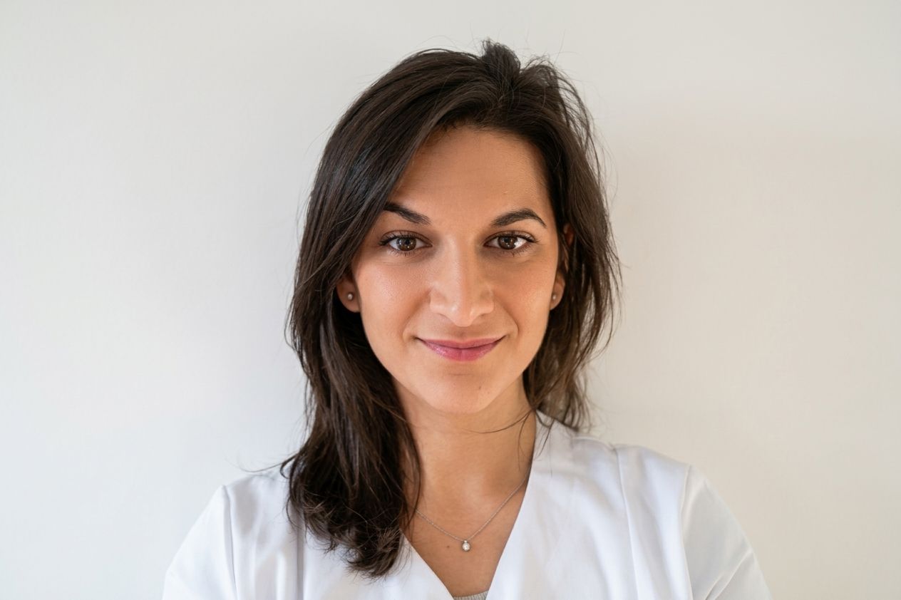 Déborah Levy, osteopath, in a white practitioner’s tunic, smiling at the camera.