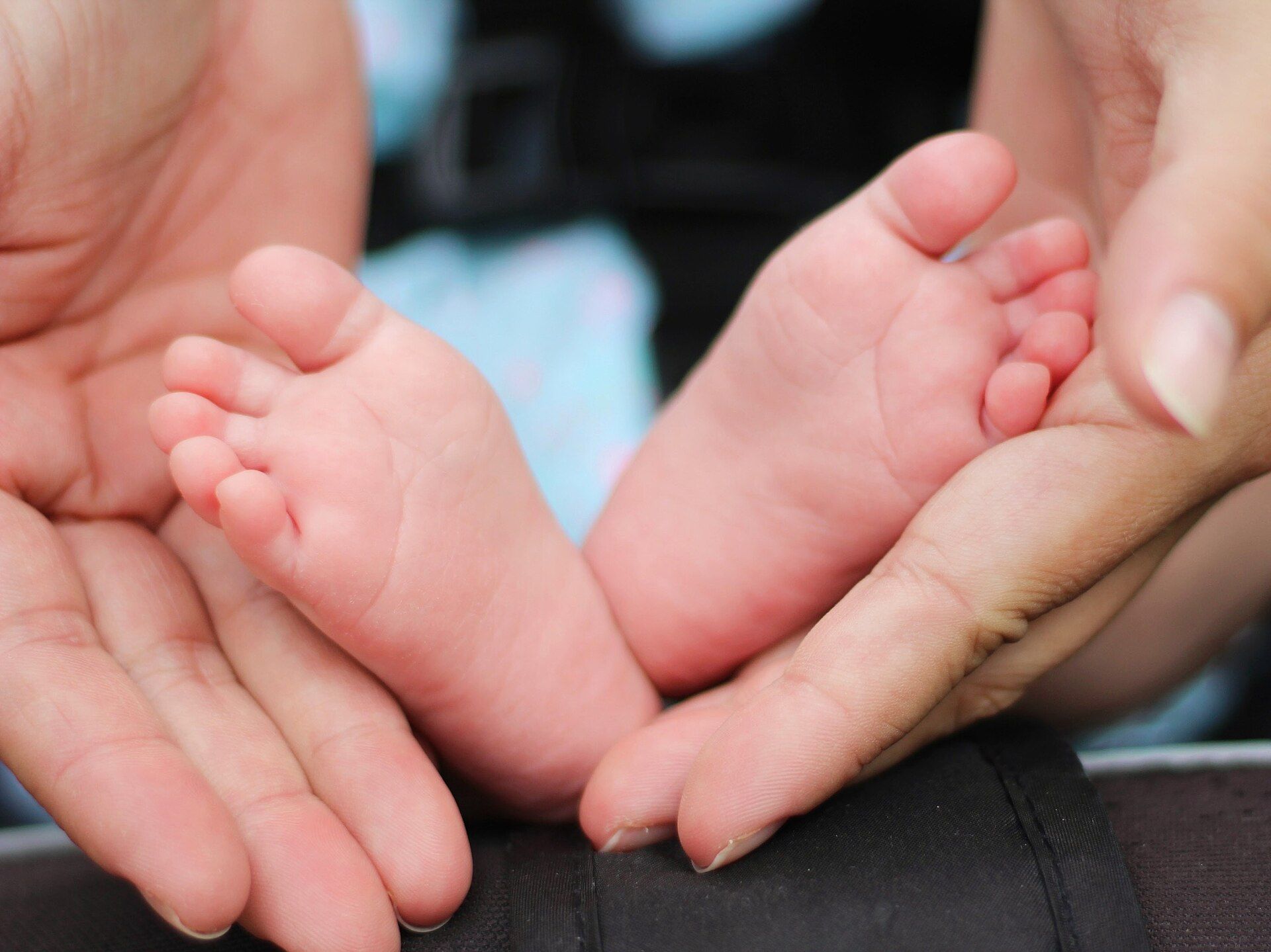 A mother's hands gently holding her newborn's feet.