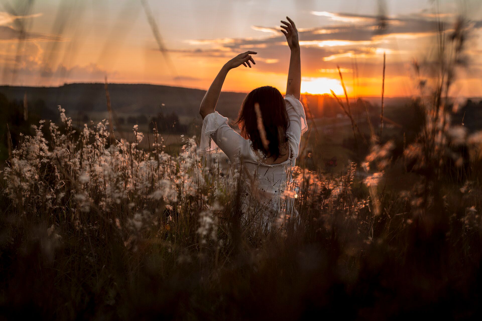 A woman stretching her arms towards the sky at sunrise, in a field.