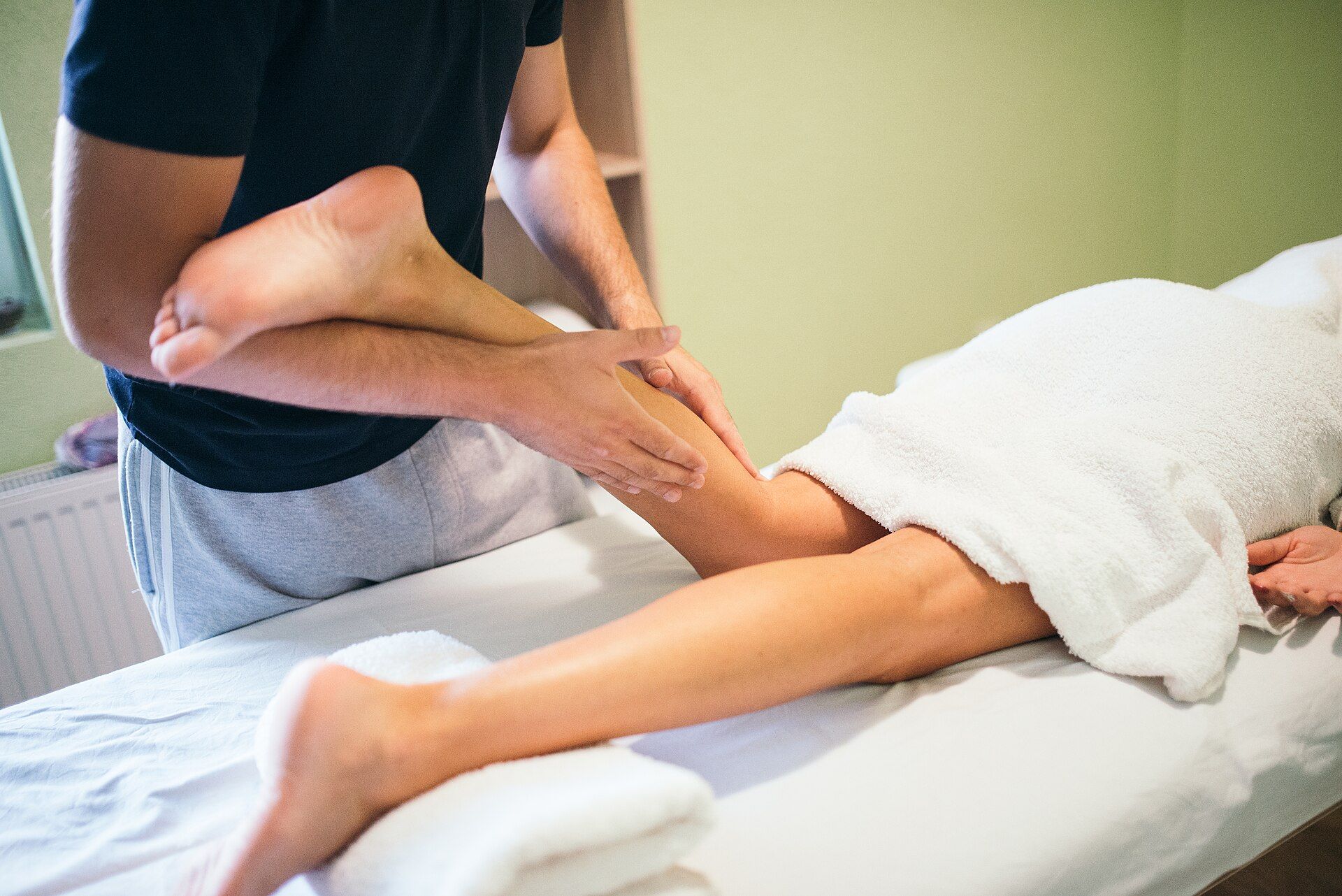 A manual therapy session on the leg of a patient lying on a treatment table.
